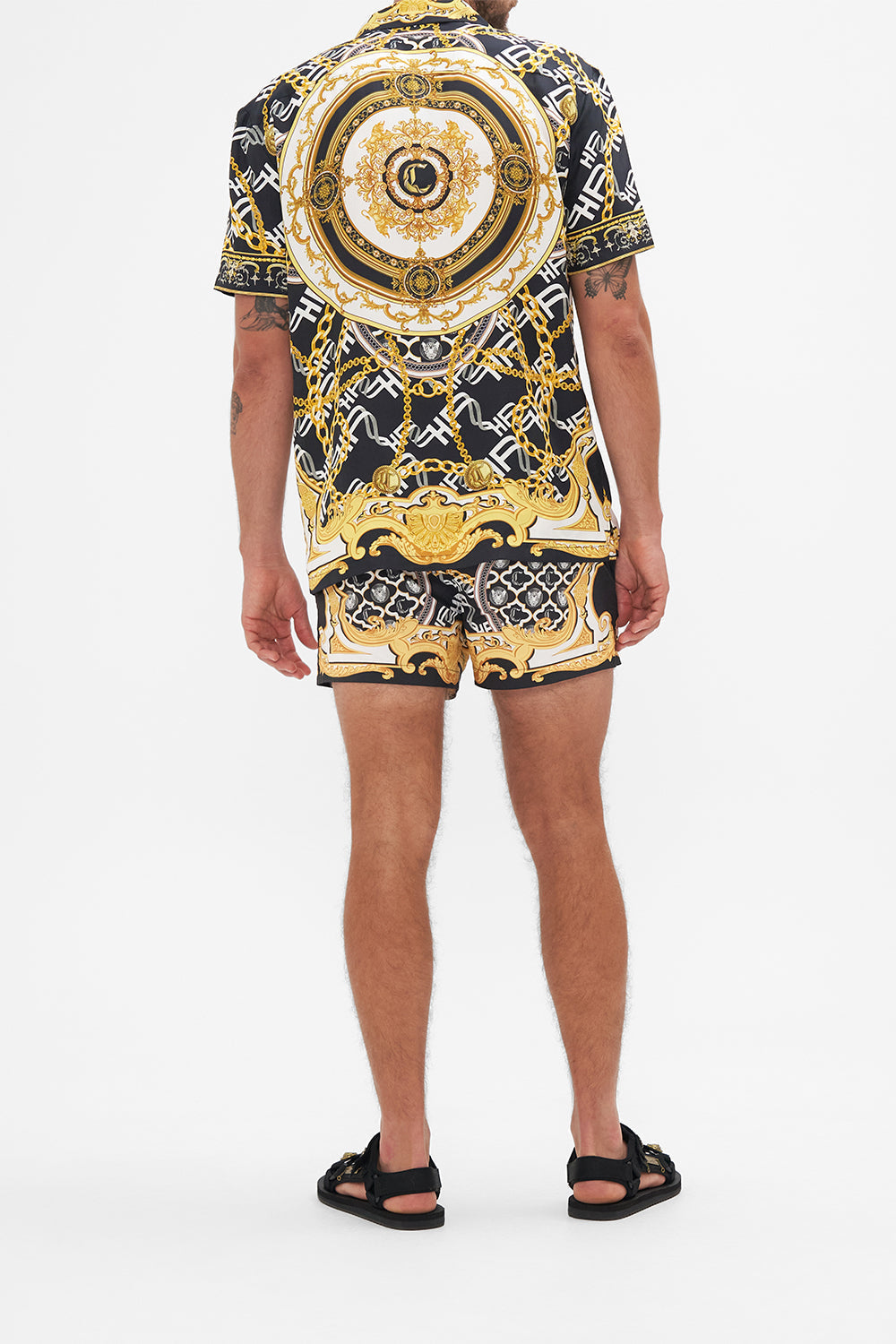 Back view of model wearing Hotel Franks by CAMILLA mens silk short sleeve camp collared shirt in black and gold Tether Me Not print