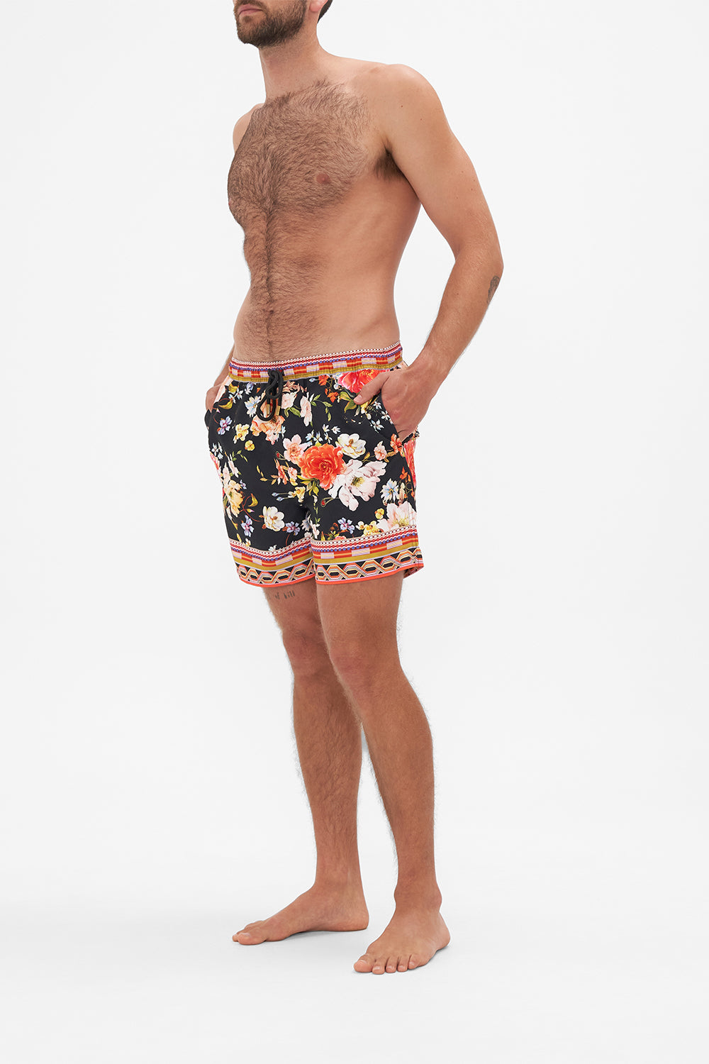 Side view of model wearing Hotel Franks by CAMILLA mens black floral print boardshorts in Secret History print