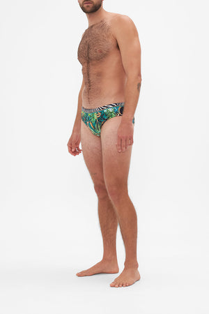Side view of model wearing Hotel Franks by CAMILLA mens green swim briefs in Sing My Song Print