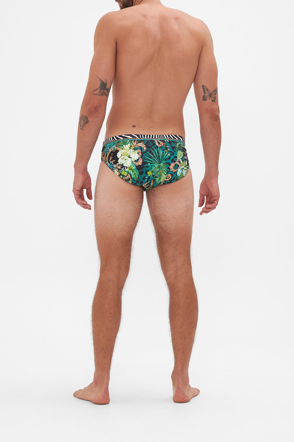 Back view of model wearing Hotel Franks by CAMILLA mens green swim briefs in Sing My Song Print