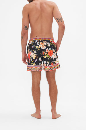 Back view of model wearing Hotel Franks by CAMILLA mens black floral print boardshorts in Secret History print