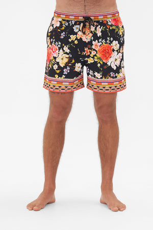 Crop view of model wearing Hotel Franks by CAMILLA mens black floral print boardshorts in Secret History print