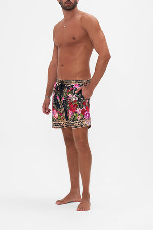 Side view of model wearing Hotel Franks by CAMILLA mens boardshorts in Reservation For Love print 