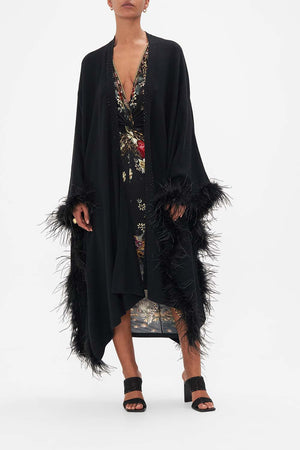 Front view of model wearing CAMILLAmerino wool knit throw over with feathers in A Night At The Opera print